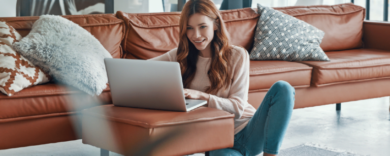 Mujer joven sonriente buscando información sobre crédito hipotecario con subsidio desde su laptop en casa